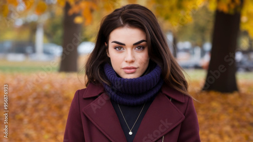 A woman wearing a burgundy coat and blue scarf stands outside with wind blowing her hair. Concept of autumn fashion and beauty outdoors. 