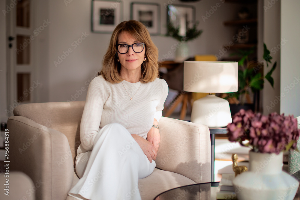 Portrait of a mature woman wearing white sweater and pants and sitting in her modern home Portrait of a mature woman wearing white sweater and pants and sitting in her modern home