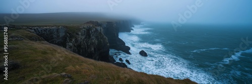 Coastal cliffs meeting the ocean under a misty dawn sky, creating a serene and dramatic seascape view.
