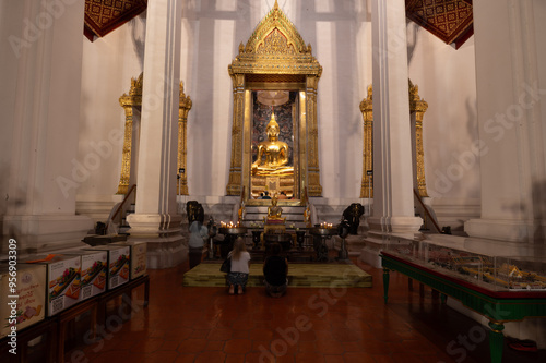 Thailand, August 11, 2024, Wat Suthat Thep Wararam Ratchaworamahawihan, Visitors pray before a golden Buddha statue inside a beautifully decorated temple in Thailand during the evening prayer session photo