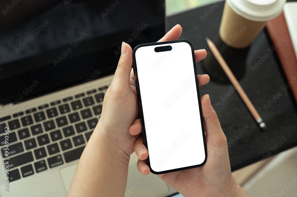 Close up image of woman holding smartphone with blank screen and using laptop Close up image of woman holding smartphone with blank screen and using laptop