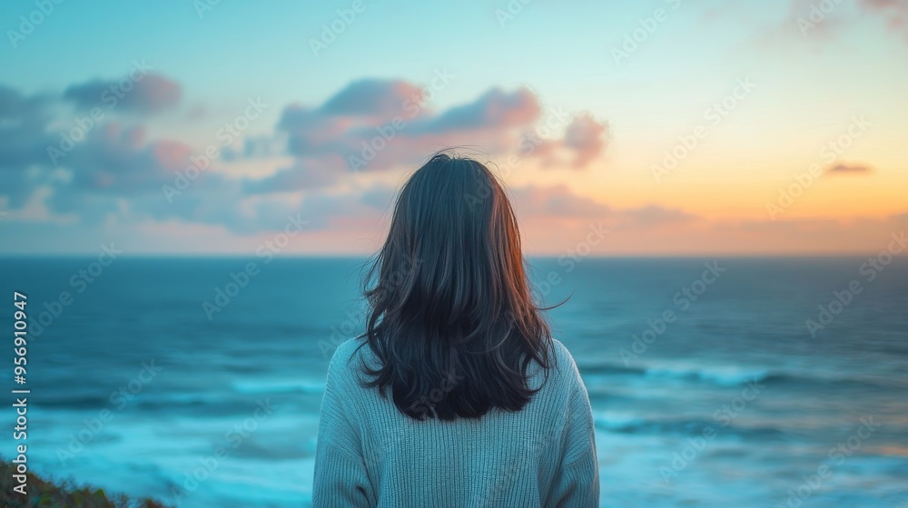 Obraz premium A Japanese woman standing by the ocean, the sky above filled with pastel colors of early morning