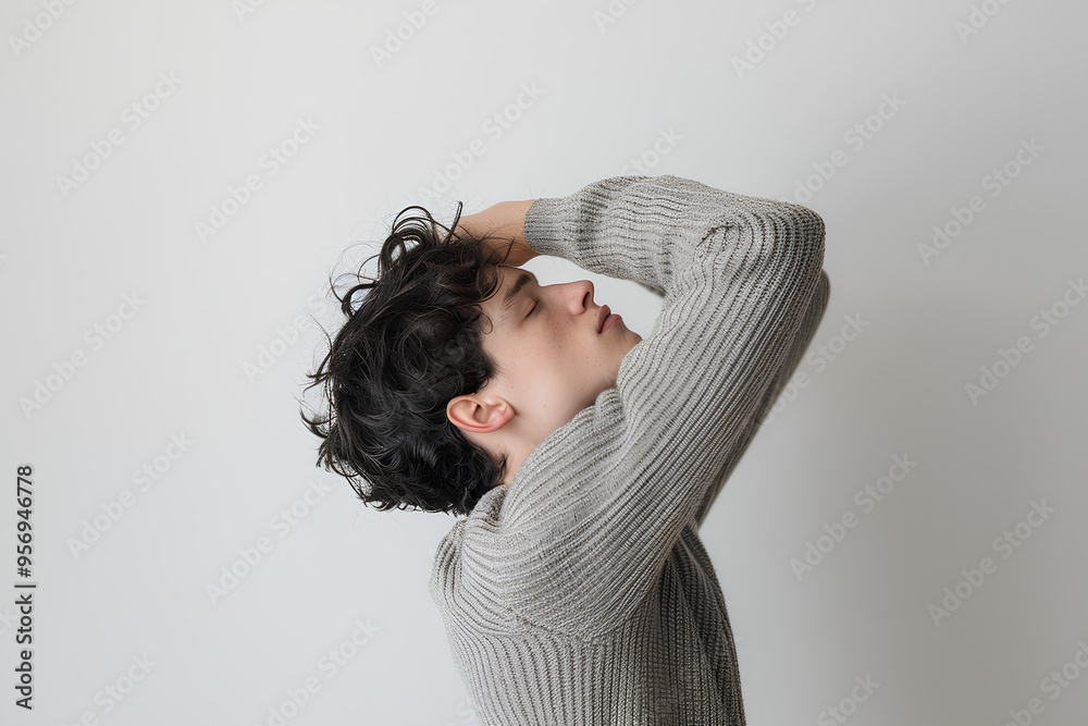 Fototapeta premium A man holding under his armpit, his sweater is grey in color with a white background, his arm is raised up to the top of his head