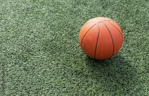 Orange basket ball lying on green playground.