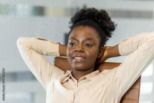 Confident African American businesswoman relaxing with hands behind head in office chair. Business attire suggests professional environment, promoting concepts of success, relaxation, and career