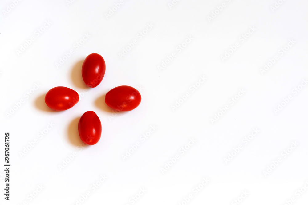 Four red cherry tomatoes on a white flat background, the tomatoes are positioned like petals of a flower in the upper left corner leaving free space on the right side Four red cherry tomatoes on a white flat background, the tomatoes are positioned like petals of a flower in the upper left corner leaving free space on the right side