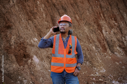 a young asian male construction worker makes a mobile phone call and reports the results of his work