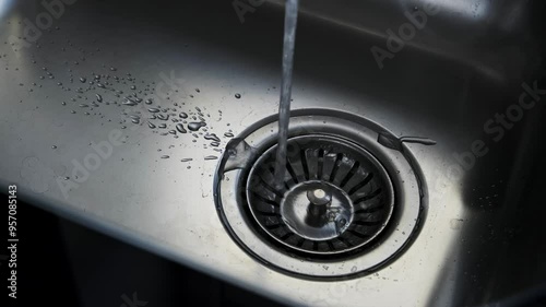 Close-up of water flowing into a stainless steel kitchen sink with droplets around the drain, highlighting cleanliness and modern kitchen design.