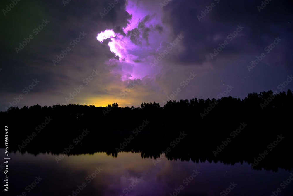 Fototapeta premium lightning strikes at night behind the clouds in the reflection of the lake in autumn