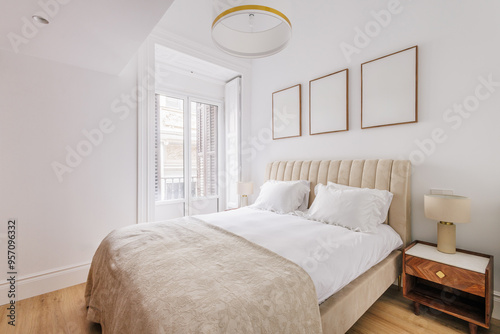 A bright bedroom with a large window, white walls, and wooden floor