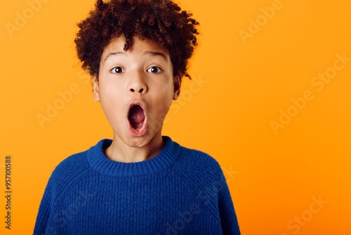 Astonished young african american boy with wideeyed expression and open mouth against a vibrant orange background photo