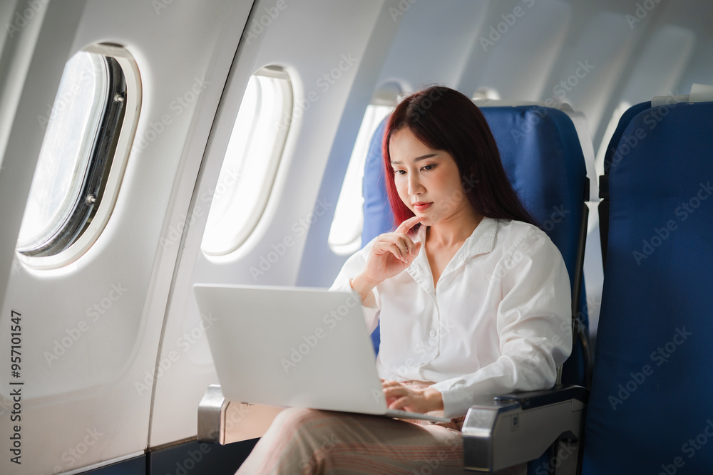 Focused at 30,000 Feet: A young Asian businesswoman engrossed in her laptop, capitalizing on flight time for productivity amidst the clouds. Focused at 30,000 Feet: A young Asian businesswoman engrossed in her laptop, capitalizing on flight time for productivity amidst the clouds.