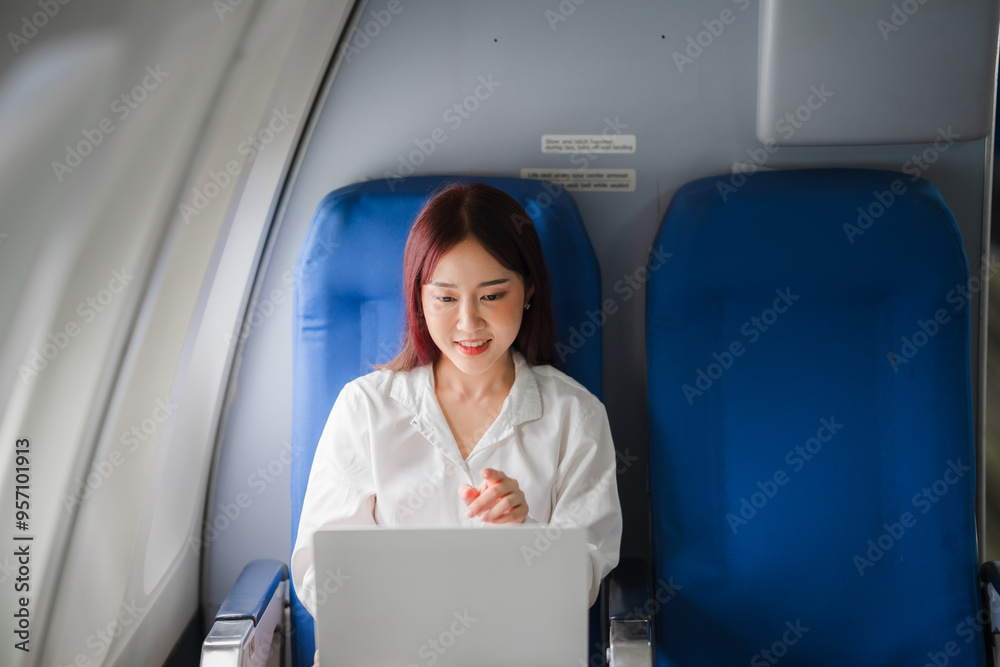 In-Flight Productivity: Young Asian woman working on laptop while seated in airplane cabin In-Flight Productivity: Young Asian woman working on laptop while seated in airplane cabin