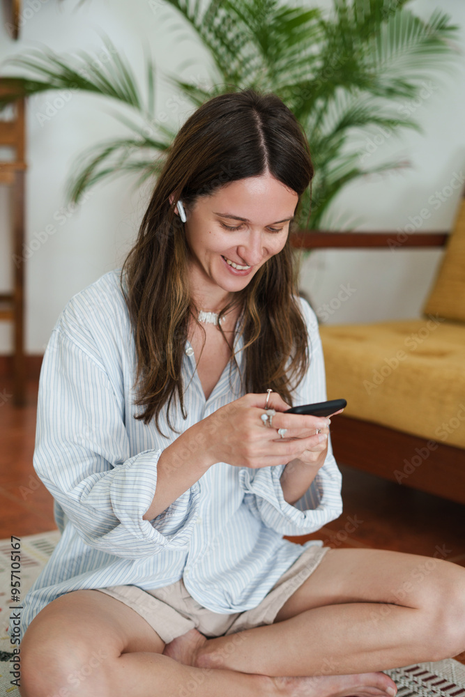 Young Woman Smiling While Using Phone with Wireless Earbuds Young Woman Smiling While Using Phone with Wireless Earbuds
