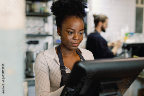 Cashier or waitress using cash register at counter near blurred waiter