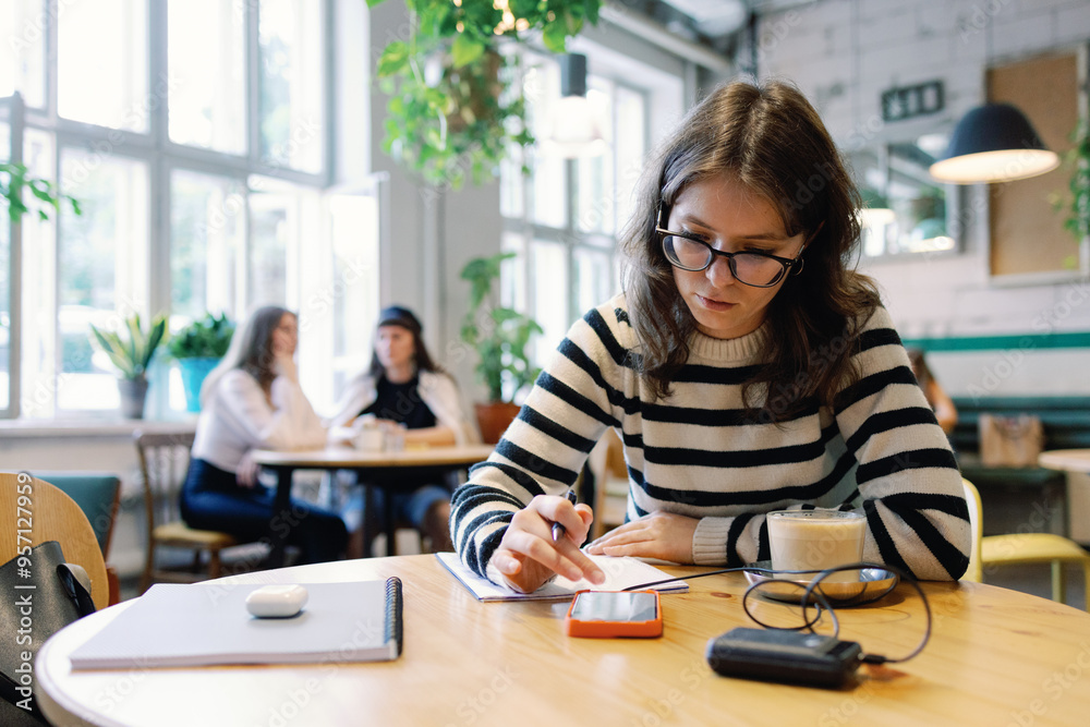 Female student watching smartphone at table near visitors in cafe Female student watching smartphone at table near visitors in cafe