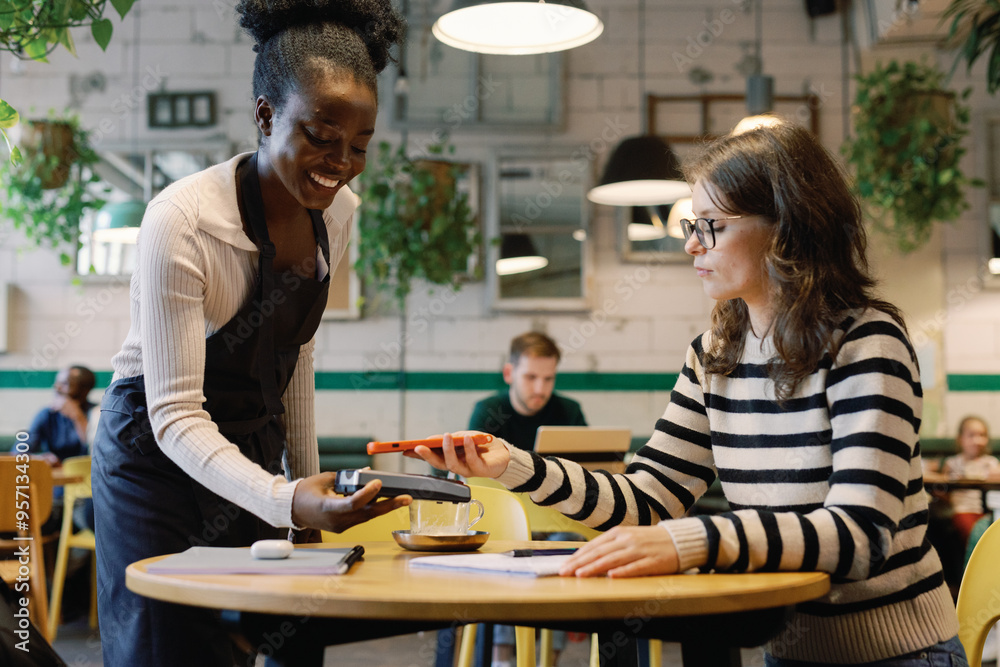 Woman paying for order with mobile app to smiling waitress in cafe Woman paying for order with mobile app to smiling waitress in cafe