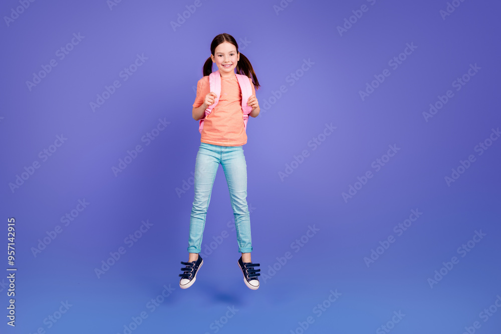 Full length photo of lovely small girl jump flying backpack dressed stylish red garment isolated on violet color background Full length photo of lovely small girl jump flying backpack dressed stylish red garment isolated on violet color background