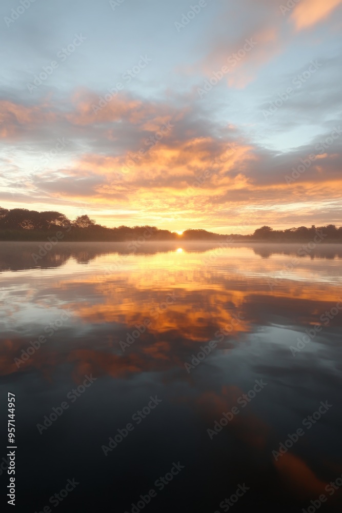 Fototapeta premium Mirror reflection of a sunset on a lake, vibrant colors and clouds, tranquil atmosphere