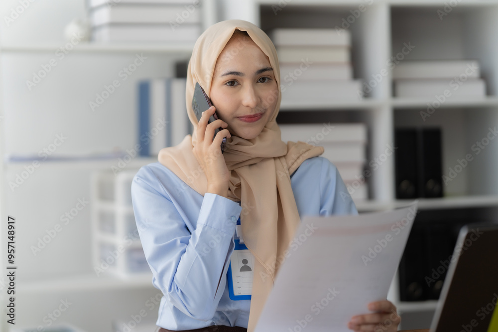 Focused Professional Grace: A Muslim businesswoman wearing a hijab conducts business with a serene smile, multitasking between a phone call and documents in her modern office. Focused Professional Grace: A Muslim businesswoman wearing a hijab conducts business with a serene smile, multitasking between a phone call and documents in her modern office.