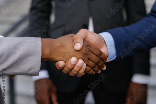 Two businesspeople shaking hands outdoors in front of colleague