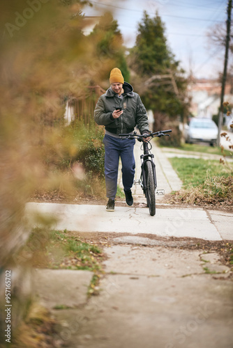 Man Using Cell Phone While Walking Bike Down Street