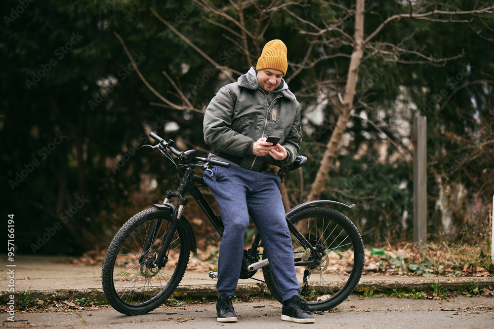 Fototapeta premium Man Texting on Cell Phone While Leaning on a Mountain Bike