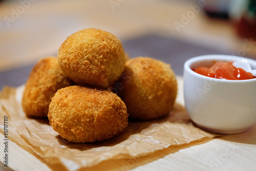 Homemade crocket from potato with filling sausages on wooden board with ketchup sauce. Side view. Close up.