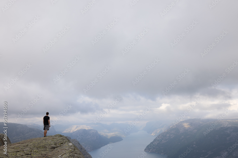 Fantasy Adventure Composite with a Man on top of a Mountain Cliff with Dramatic Landscape in Background during Sunset or Sunrise. Landscape from Preikestolen, Norway. Way to success. Fantasy Adventure Composite with a Man on top of a Mountain Cliff with Dramatic Landscape in Background during Sunset or Sunrise. Landscape from Preikestolen, Norway. Way to success.