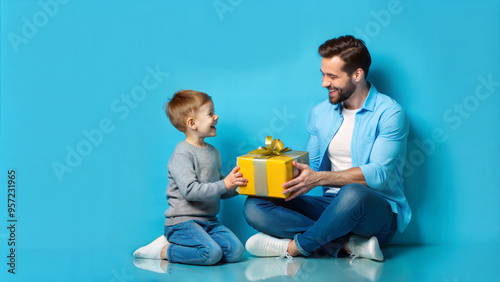 happy father and son with gift box sitting on floor on blue background