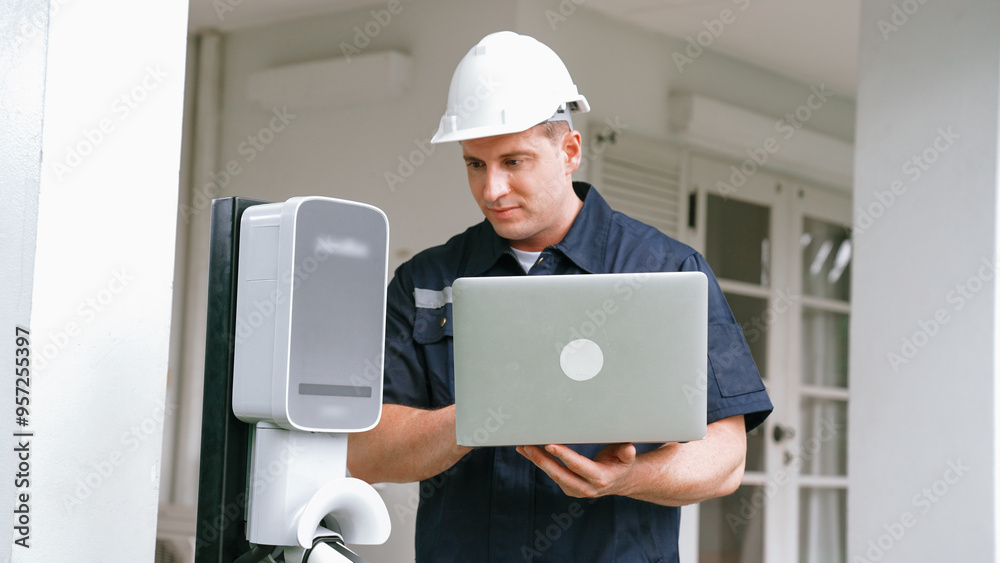 Qualified technician working on home EV charging station installation, making troubleshooting and configuration setup on charging system with laptop for EV at home. Synchronos Qualified technician working on home EV charging station installation, making troubleshooting and configuration setup on charging system with laptop for EV at home. Synchronos