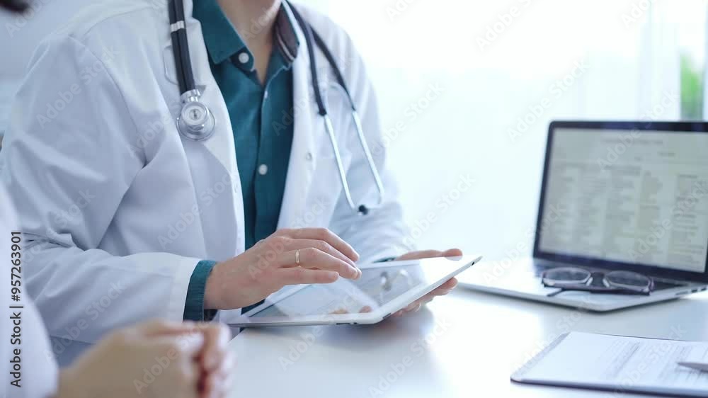 Doctor and a patient. The physician, wearing a white medical coat over a green shirt, is using tablet computer during a consultation in the clinic. Medicine concept