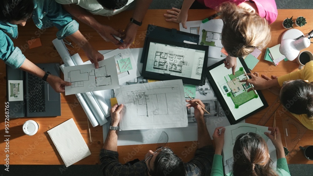 Top down of skilled business people holding tablet an looking at blueprint. Aerial view of architect engineer planning and design house design together while standing at table with laptop. Symposium. Top down of skilled business people holding tablet an looking at blueprint. Aerial view of architect engineer planning and design house design together while standing at table with laptop. Symposium.