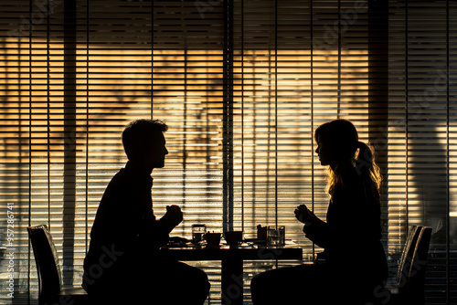 Two people engage in a conversation, silhouetted by the light filtering through blinds in a madrid setting.