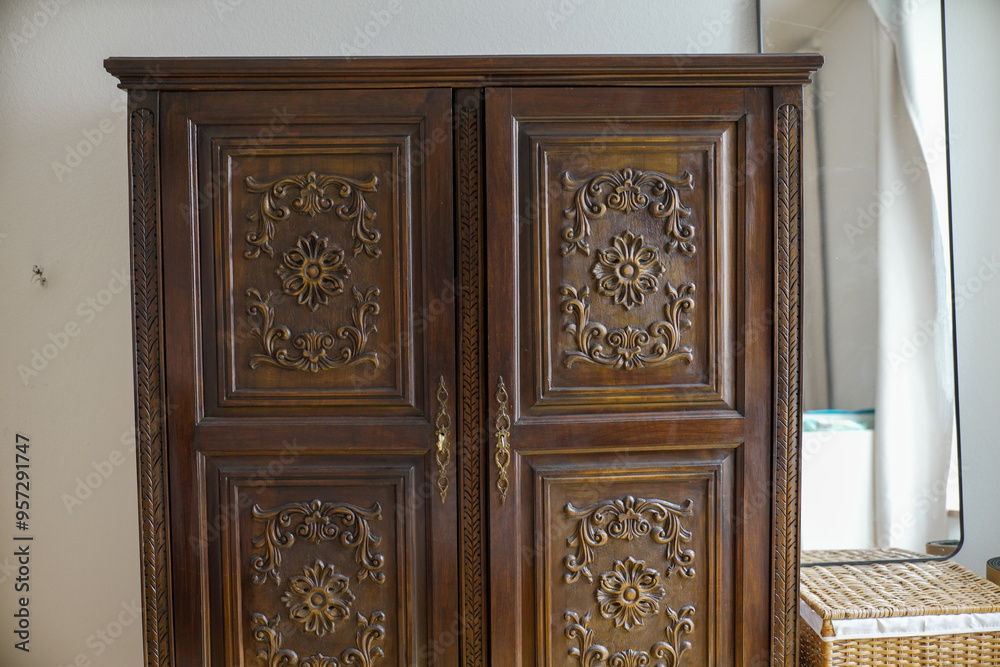 Ornate wooden wardrobe with intricate carvings and metal handles, standing against a plain wall, showcasing vintage craftsmanship and detailed design elements in home furniture Ornate wooden wardrobe with intricate carvings and metal handles, standing against a plain wall, showcasing vintage craftsmanship and detailed design elements in home furniture