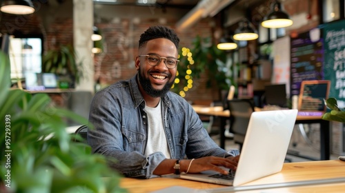 Smiling Man Working on Laptop in Modern Office with Plants and Exposed Brick Walls