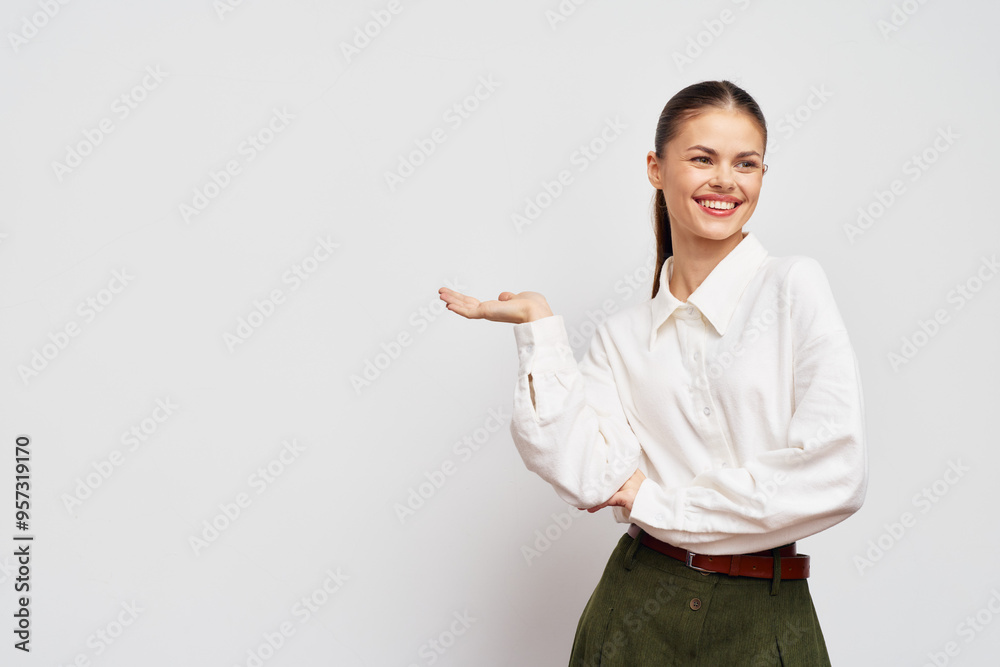Young woman smiling with open hand gesture, showcasing confidence and approachability against a light gray background Modern, stylish attire highlights professional ambiance Young woman smiling with open hand gesture, showcasing confidence and approachability against a light gray background Modern, stylish attire highlights professional ambiance