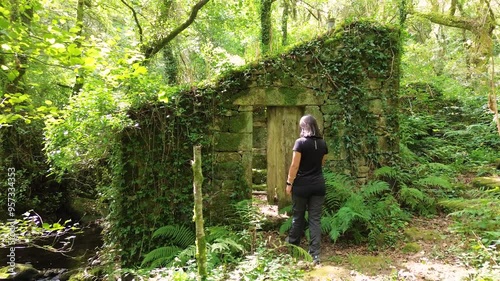 Exploring abandoned house in middle of nature surrounded by vegetation and grass. Woman explore forest. photo