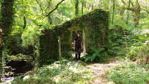 Exploring abandoned house in middle of nature surrounded by vegetation and grass. Woman explore forest. photo