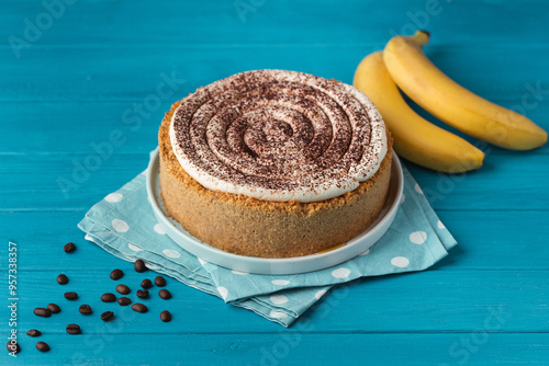 Banoffe pie filled with banana and dulce de leche and sprinkled with grated chocolate. Banana cake on white plate with glass of coffee on turquoise summer background photo