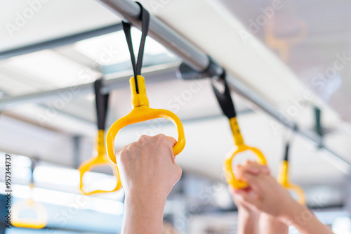Passengers holding yellow hand grips on a public transport vehicle during a morning commute photo