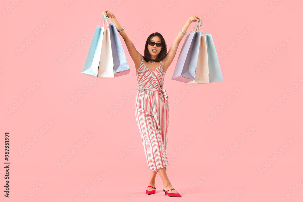 Happy beautiful young Asian woman in sunglasses with shopping bags on pink background Happy beautiful young Asian woman in sunglasses with shopping bags on pink background