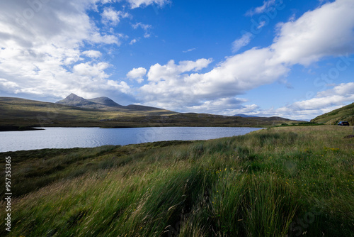 The image shows a body of water surrounded by grass and hills in Scotland. The landscape includes a lake, grassy areas, and mountainous terrain typical of the Scottish Highlands.