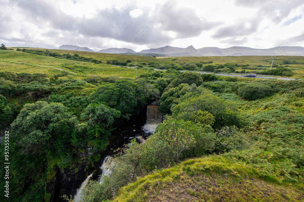 A stunning waterfall cascading down rocks in a lush green forest setting. The image captures the beauty of nature with a cloudy sky above. A stunning waterfall cascading down rocks in a lush green forest setting. The image captures the beauty of nature with a cloudy sky above.