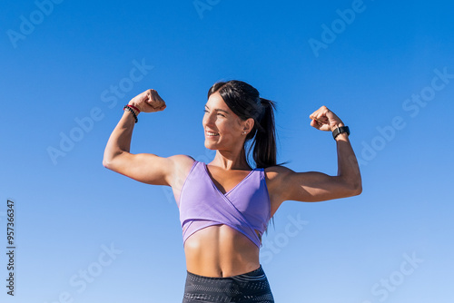 A young woman smiling and flexing her arm muscles under a blue sky
