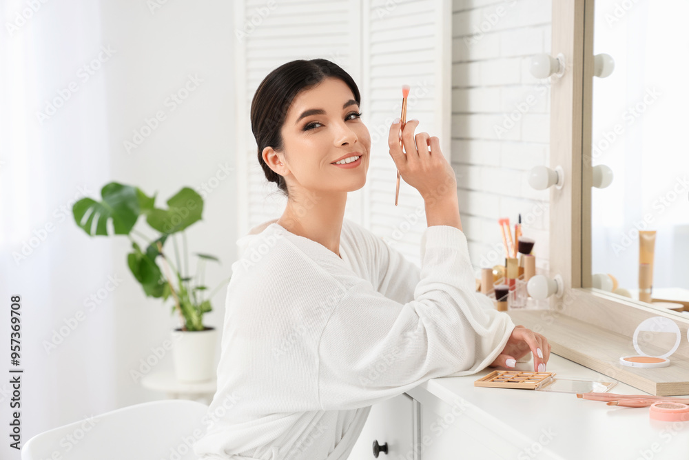 Beautiful young woman with makeup brush and different cosmetic products near mirror in salon Beautiful young woman with makeup brush and different cosmetic products near mirror in salon