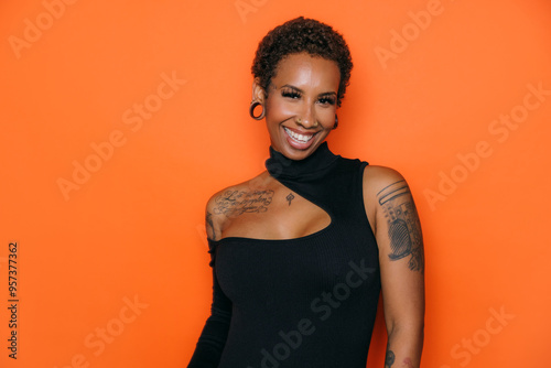 Smiling woman with short hair and tattoos against orange background photo