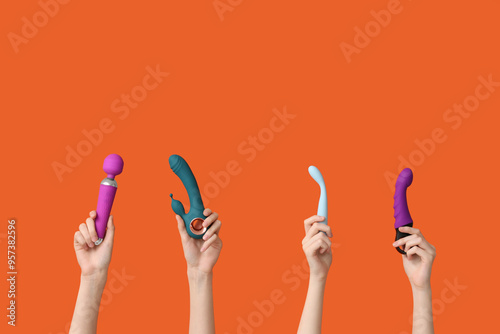 Female hands with different vibrators on orange background