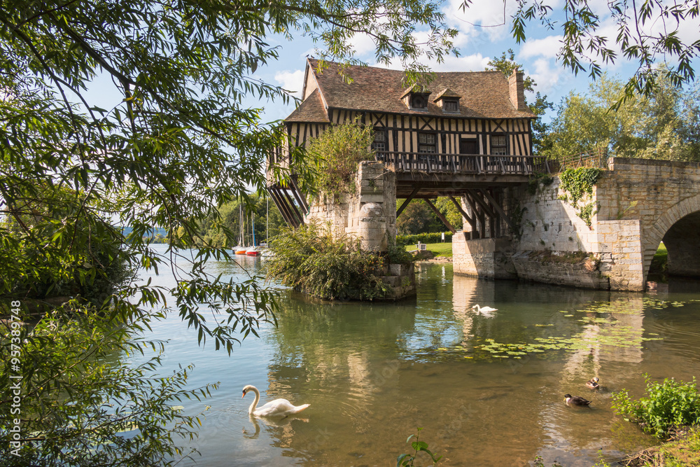 The beautiful old mill over the Seine river with swans in the foreground in Vernon, France The beautiful old mill over the Seine river with swans in the foreground in Vernon, France