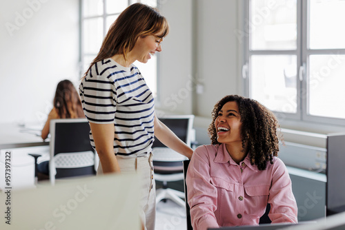 Two businesswomen sharing a laugh in busy open plan office